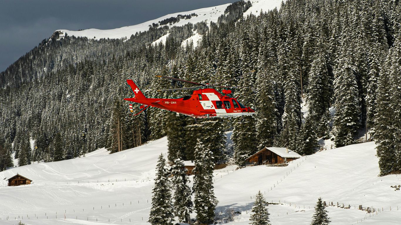 a red helicopter flying over a snow covered mountain