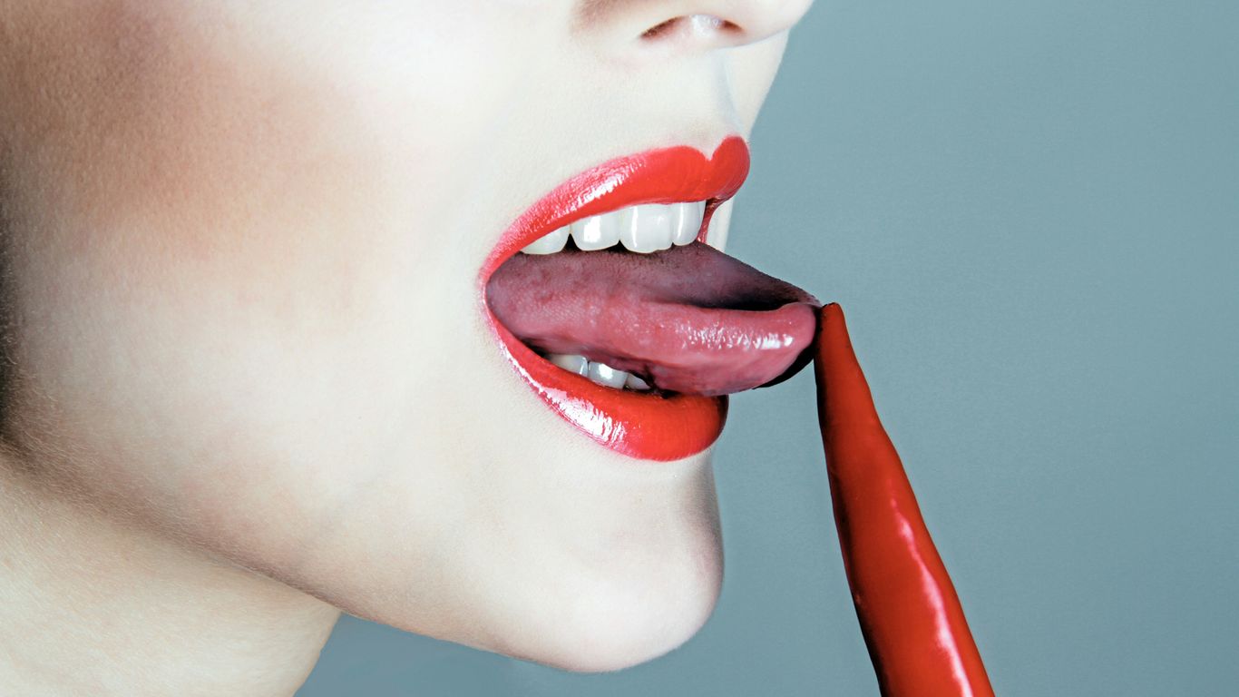 Woman licking a red chili pepper.