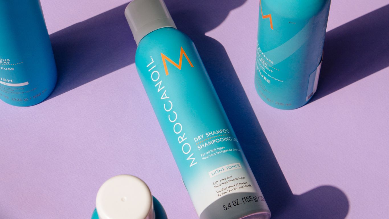 Moroccanoil hair products arranged artistically with shadows on purple background.