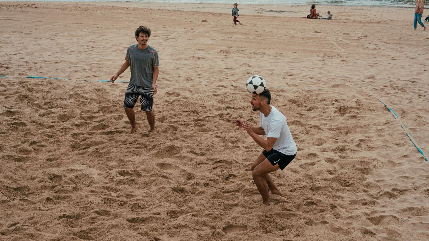 two men playing soccer on a sandy beach