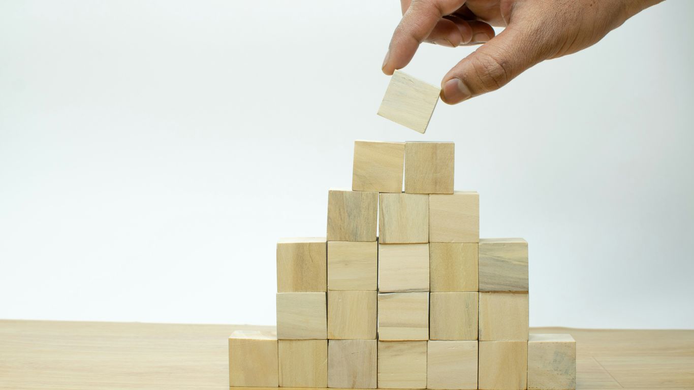 A hand is placing a piece of wood into a pyramid