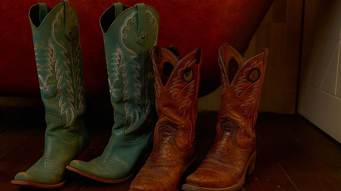 Two pairs of cowboy boots stand before a rustic bathtub.