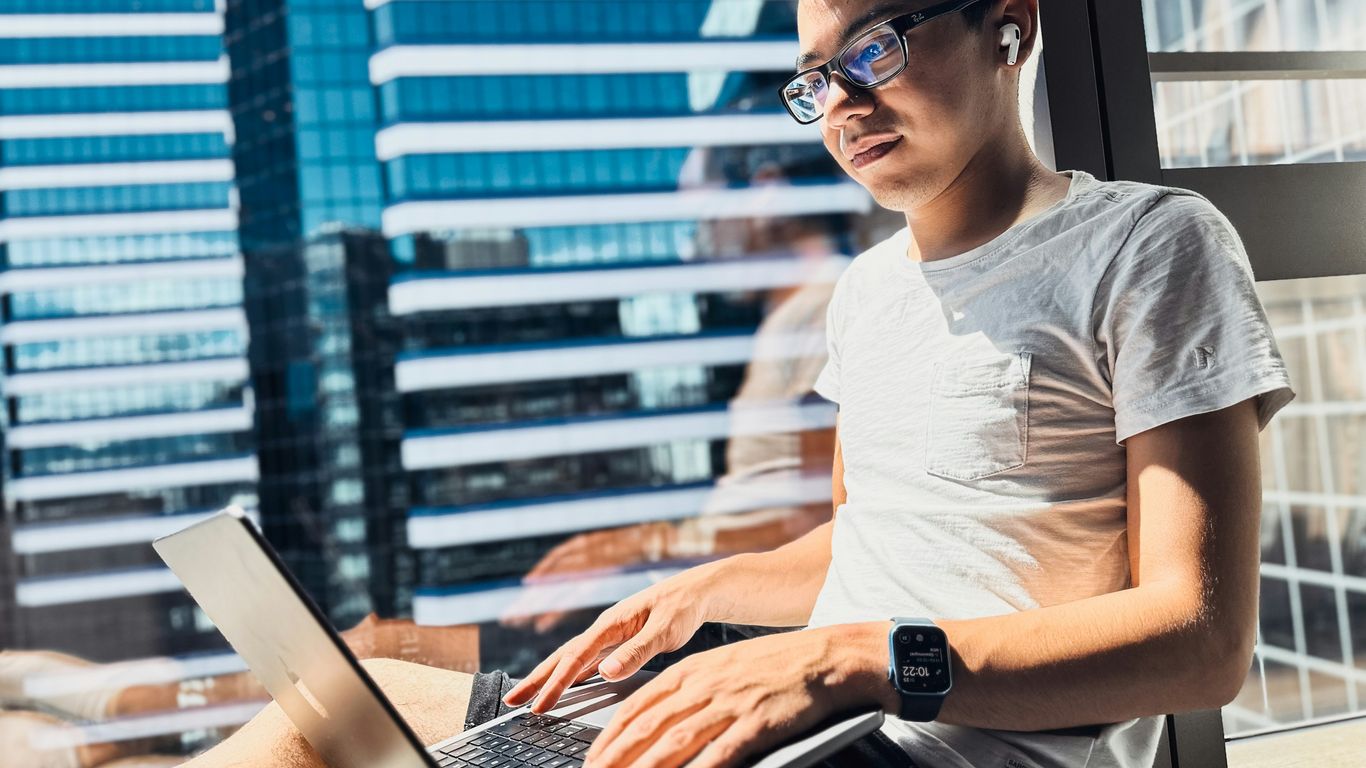 a man sitting in front of a window using a laptop computer