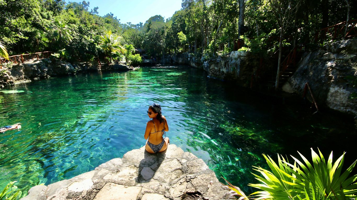 woman in black bikini sitting on rock near body of water during daytime