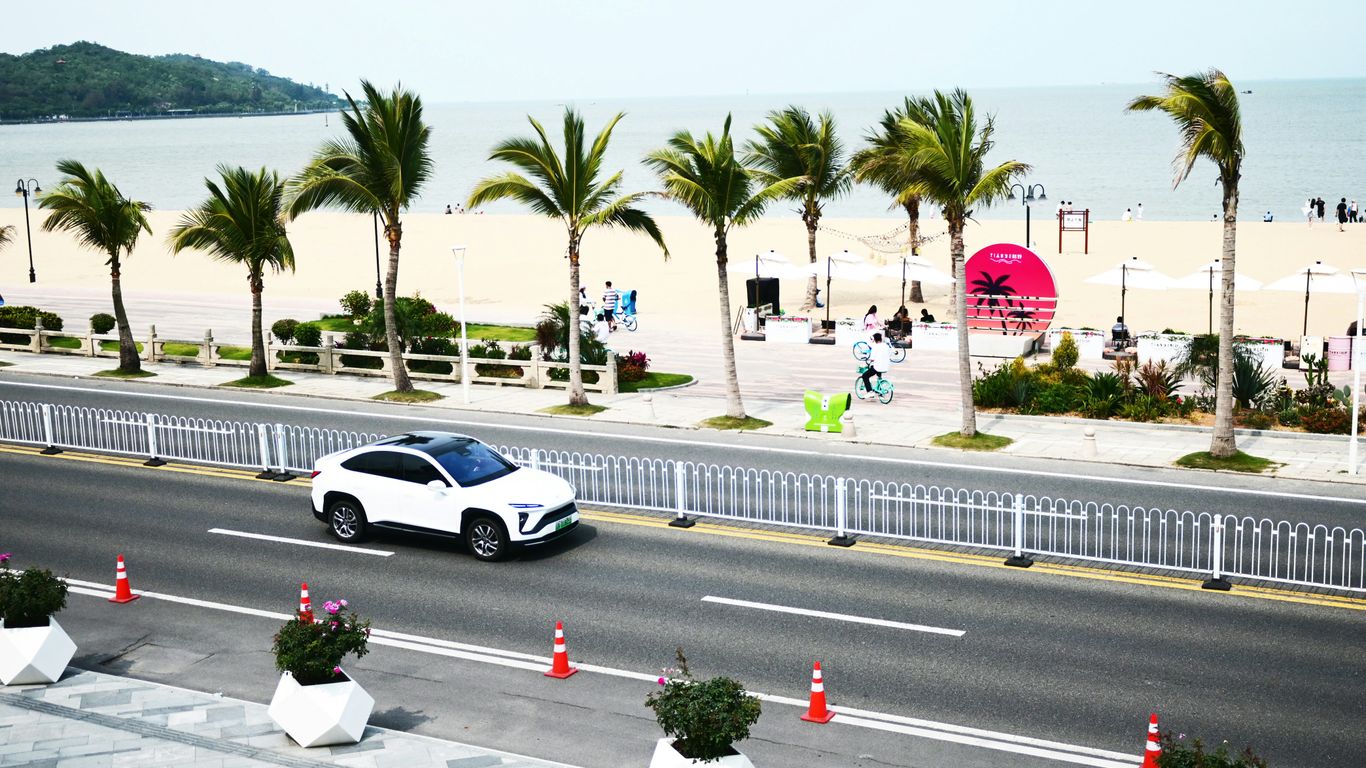 a white car driving down a street next to a beach