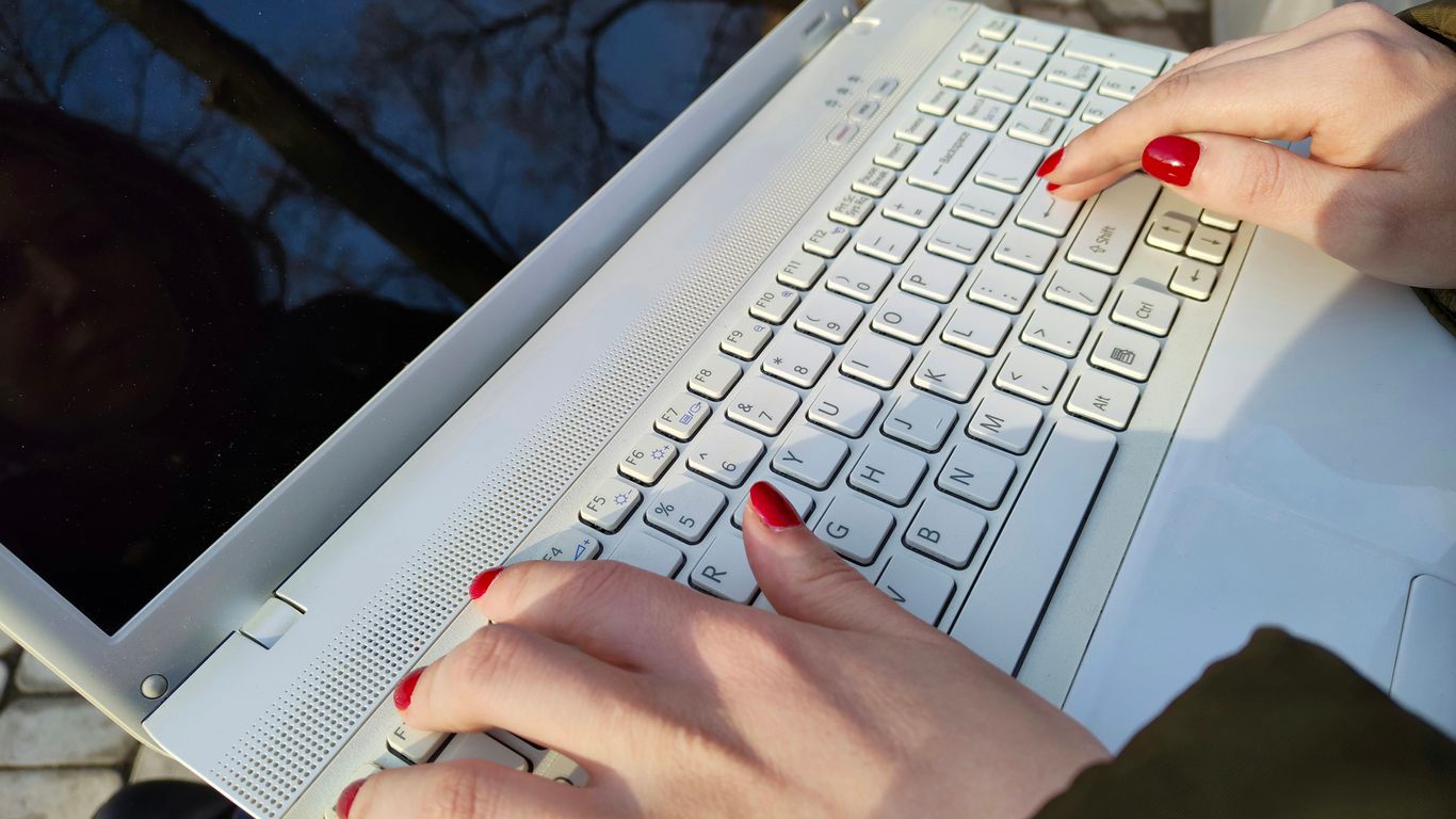 a woman is typing on a laptop outside