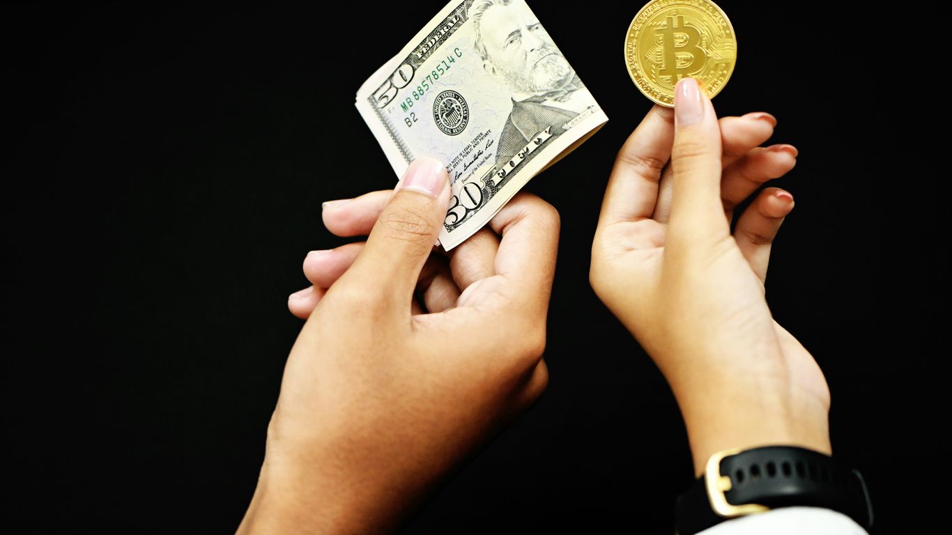 Hands holding a dollar bill and a Bitcoin on black background.