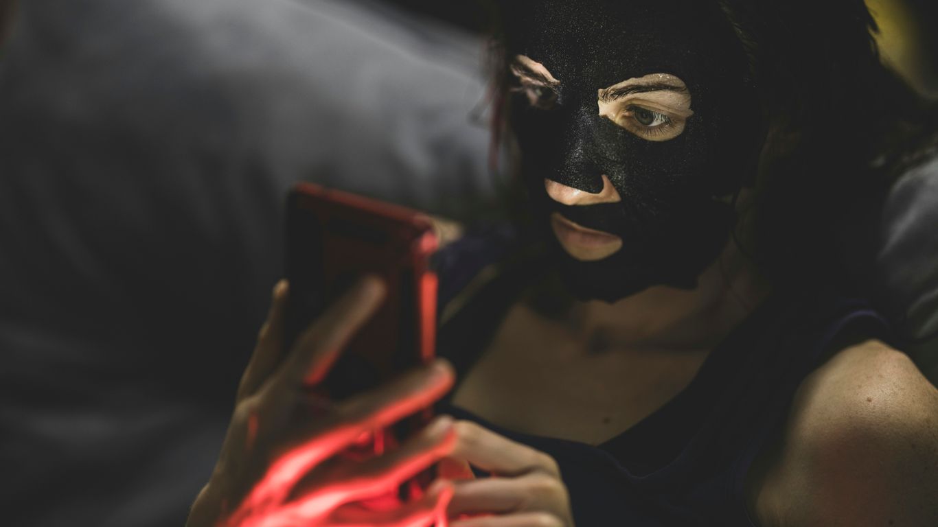 woman in black mask holding red smartphone
