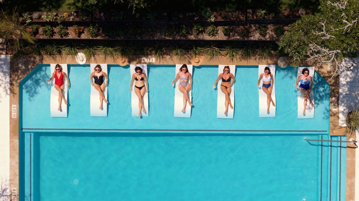 People relaxing on lounge chairs by a bright blue swimming pool.