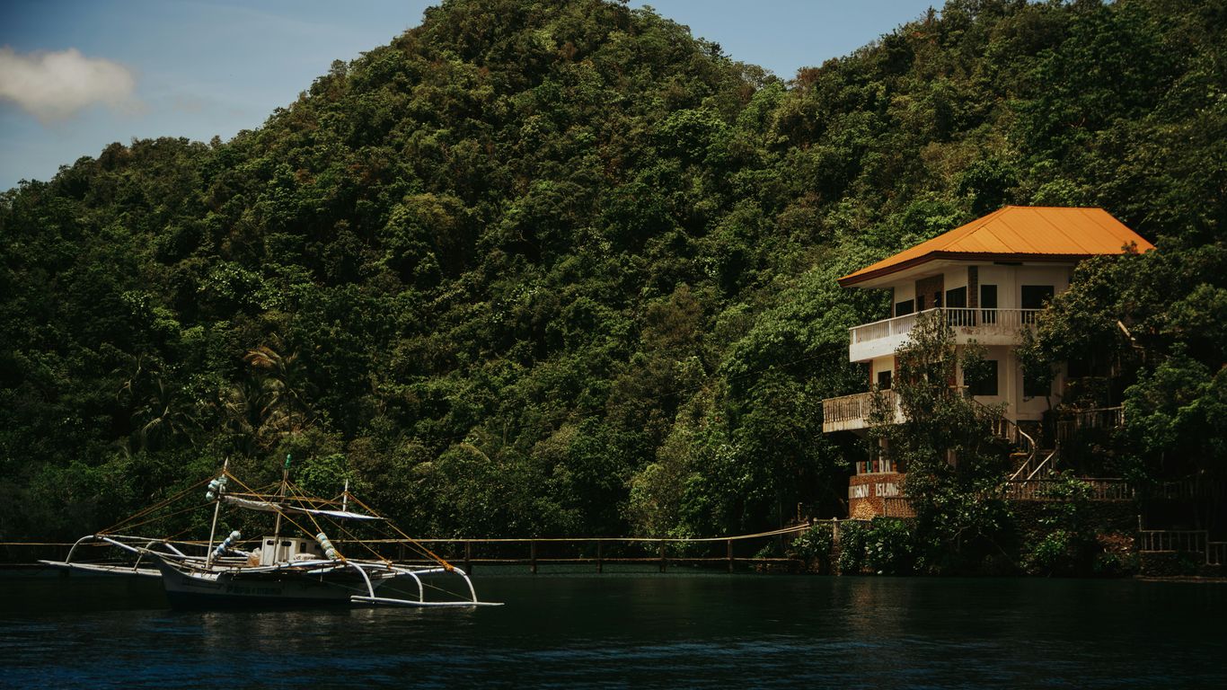 A boat sits near a house by a lush hillside.