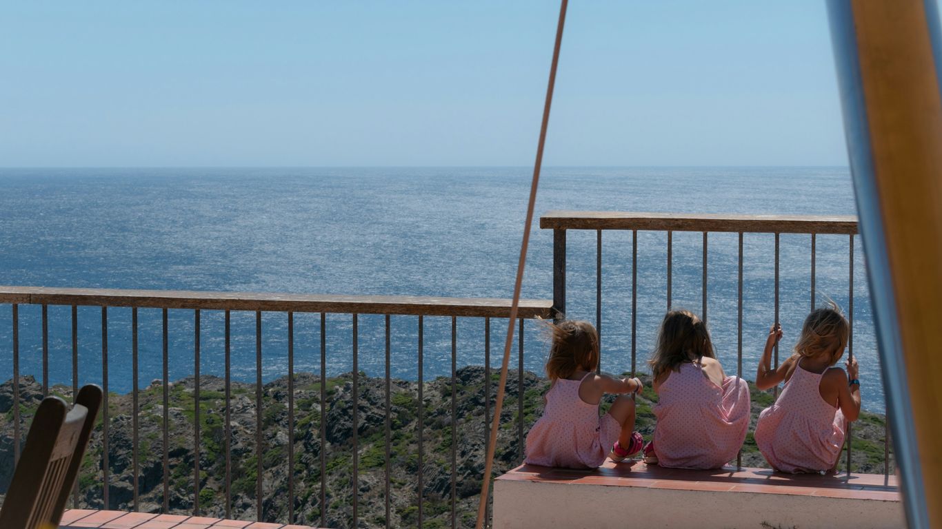 three little girls sitting on a bench looking out at the ocean