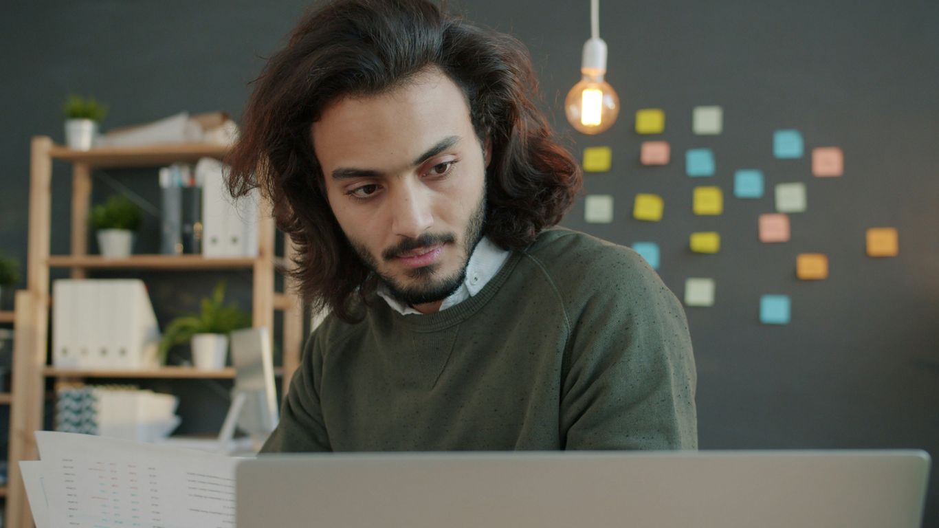 Man with long hair working on laptop in office