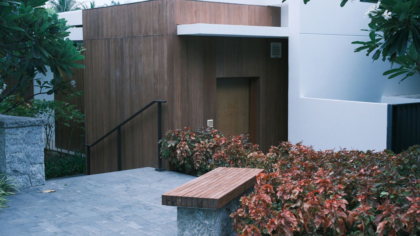 Modern building entrance with wooden accents and lush plants.