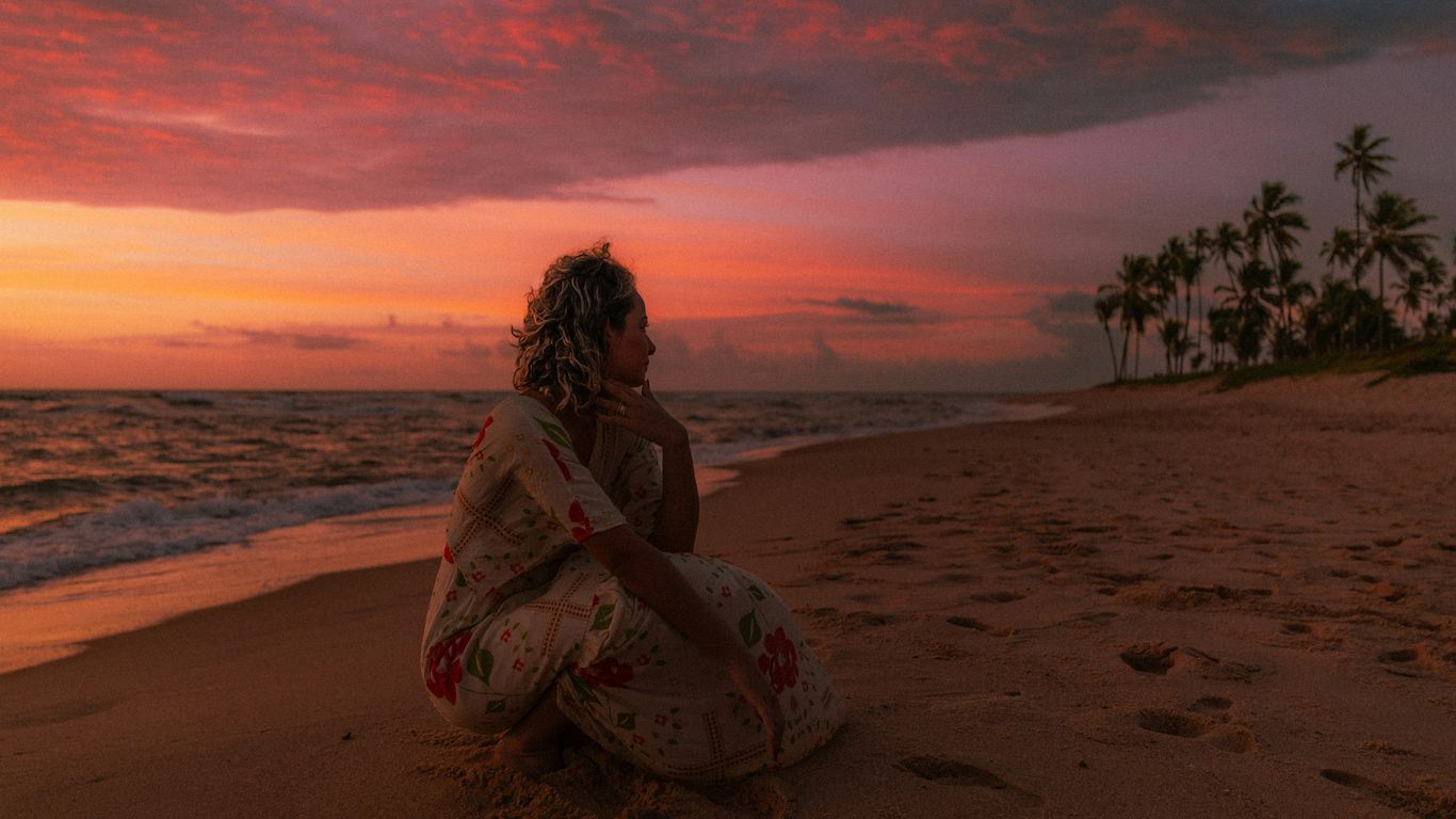 Woman sitting on beach watching sunset over ocean