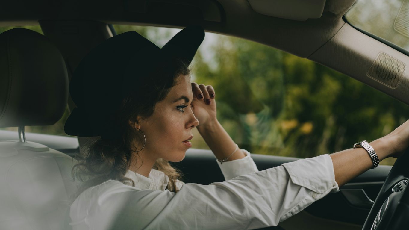 a woman sitting in a car with her hand on the steering wheel