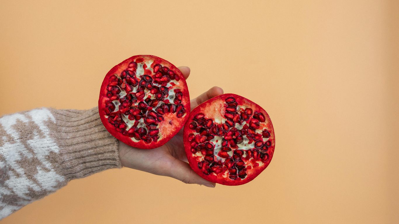 Hand holding two halves of pomegranate against peach background.