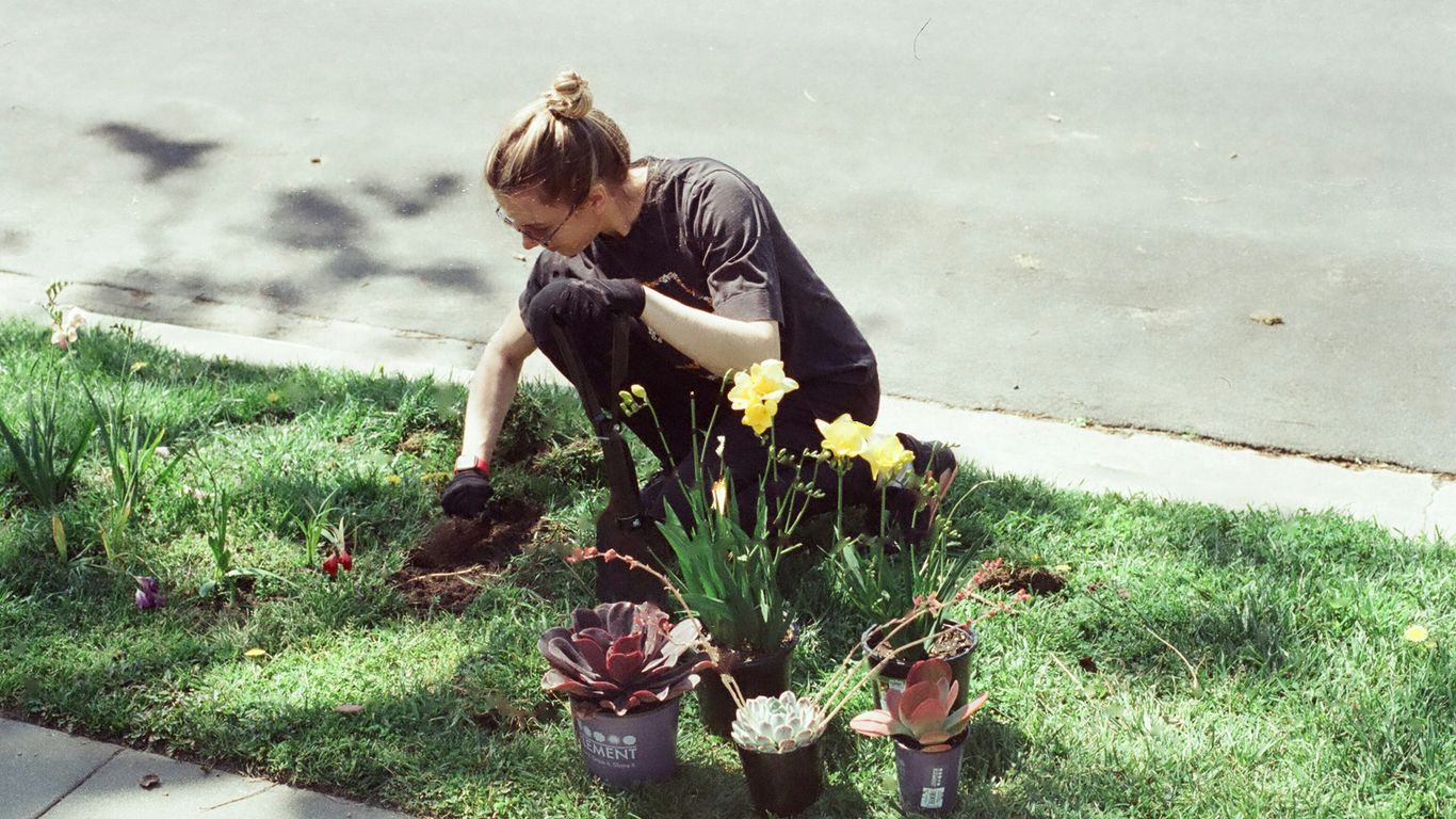 a woman kneeling down in the grass next to a potted plant