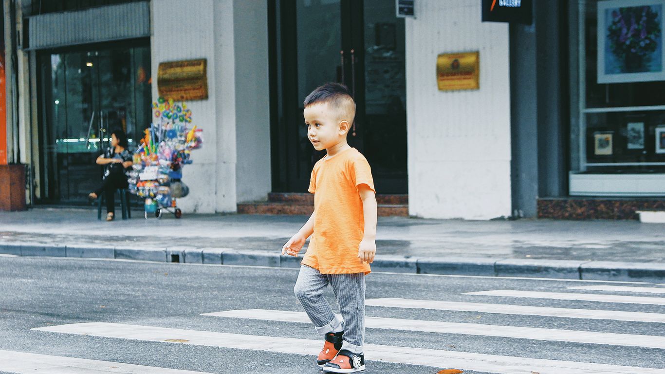 boy in orange crew neck t-shirt and blue denim jeans standing on gray concrete floor
