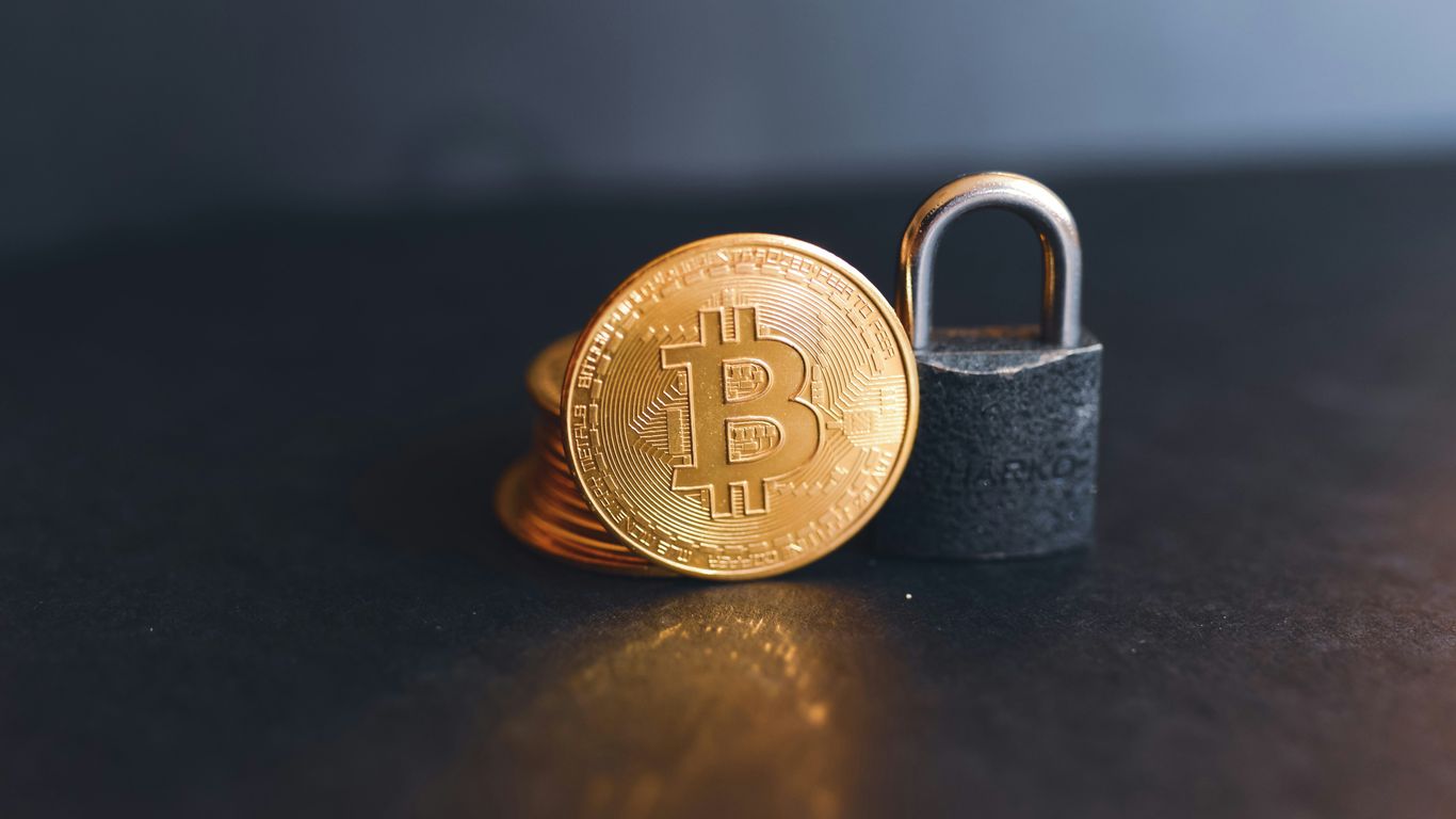 Gold Bitcoin coins next to a padlock on a surface.