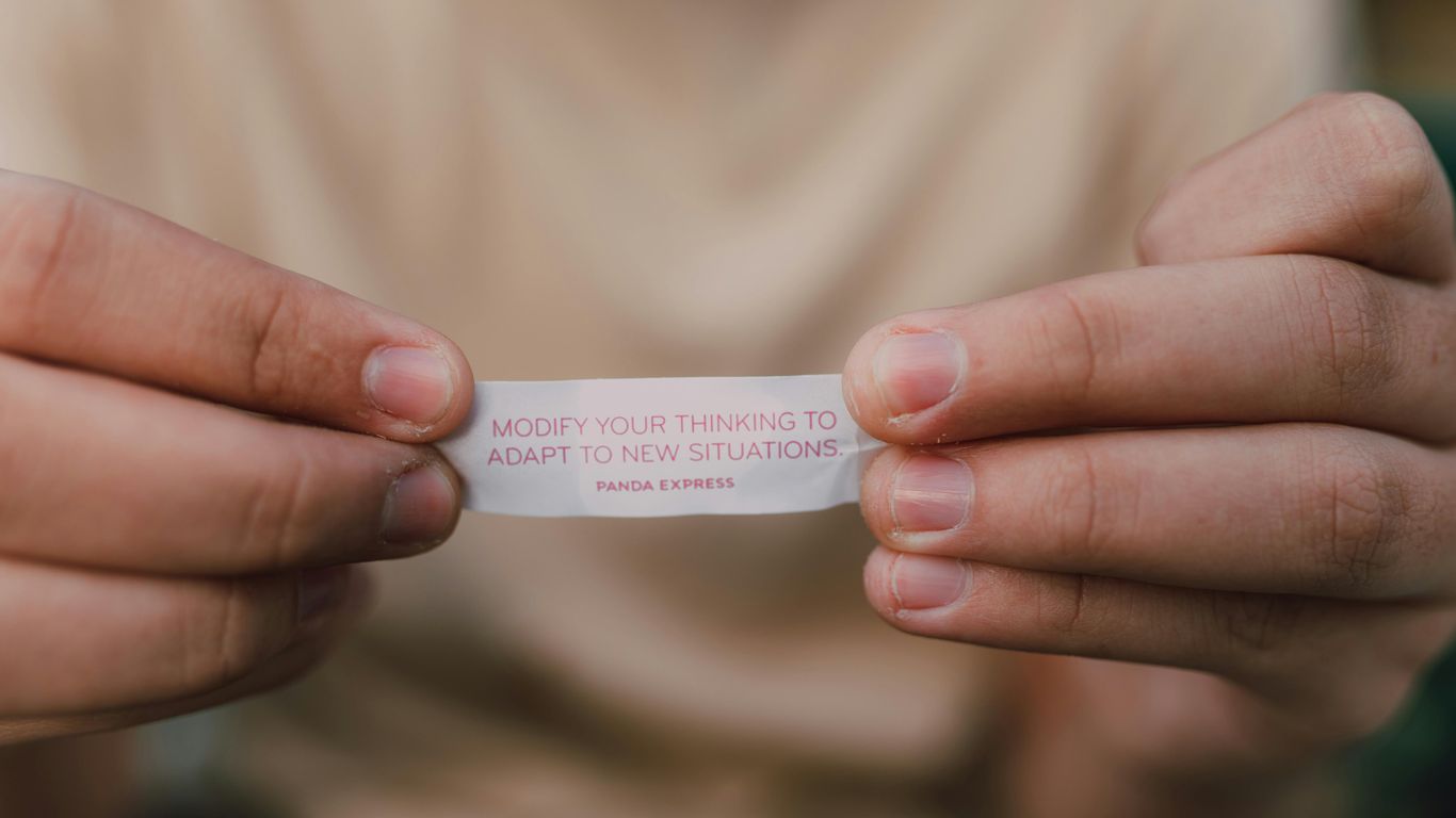 Hands holding a fortune cookie slip that says to adapt.