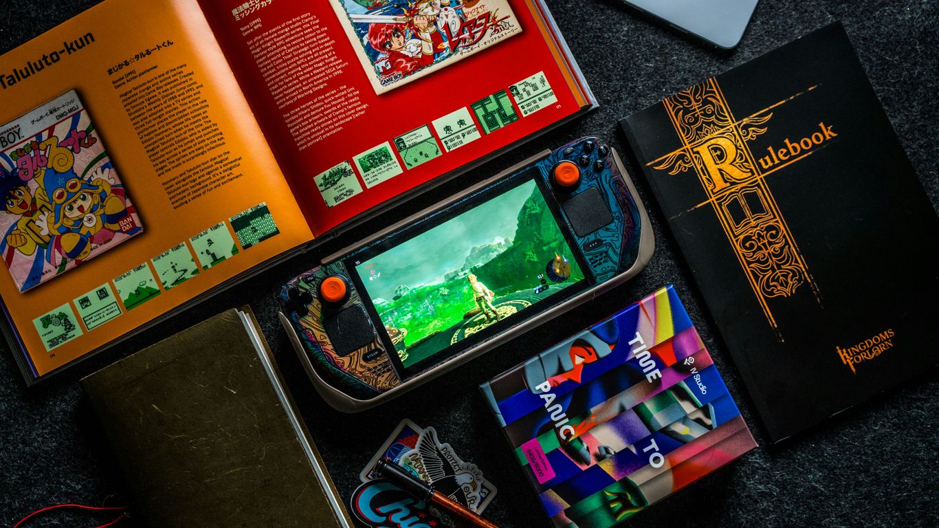 Gaming handheld, books, and phone on dark surface.