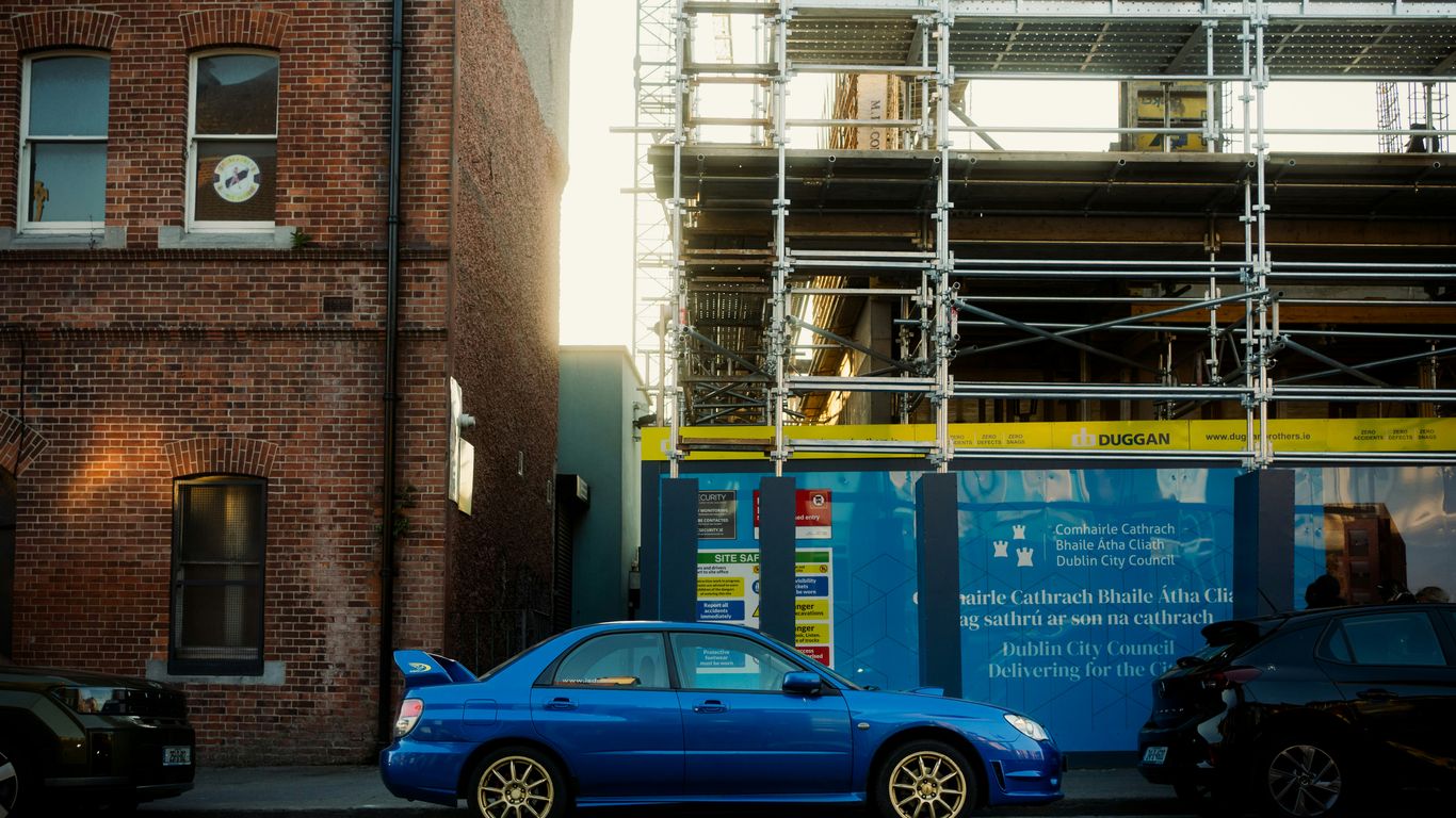 A blue car parked in front of construction.