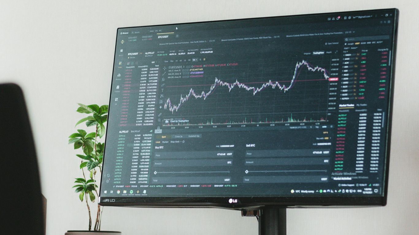 A computer monitor displaying stock market data with a plant.