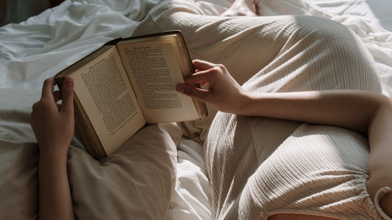 Person lying on bed reading a book in sunlight.
