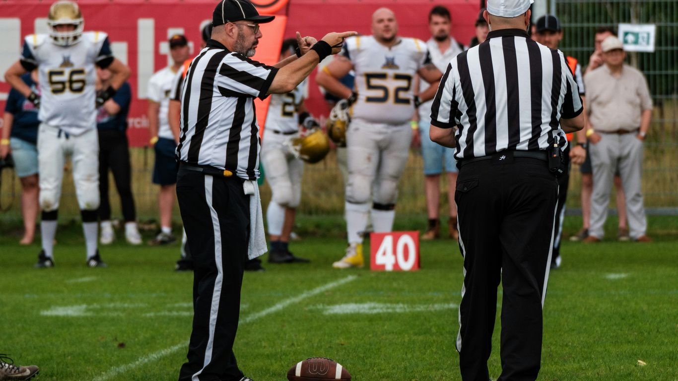 Referees on a football field with players in background.