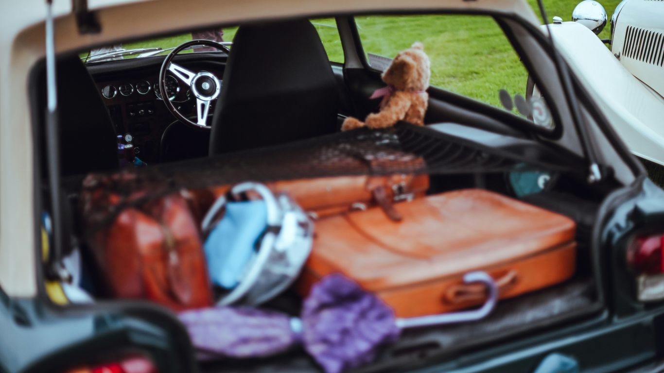 Open car trunk filled with luggage and teddy bear.
