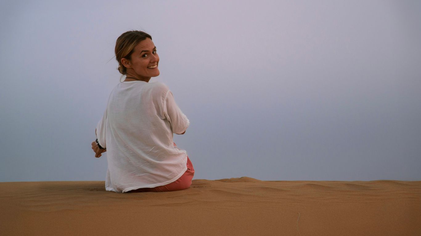 Young woman sitting on sand dune looking back