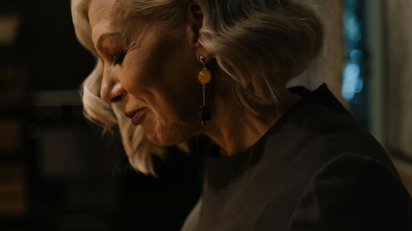 Person with short blonde hair and earrings in soft lighting.