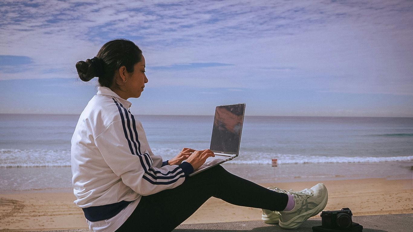 Woman works on laptop by the beach.