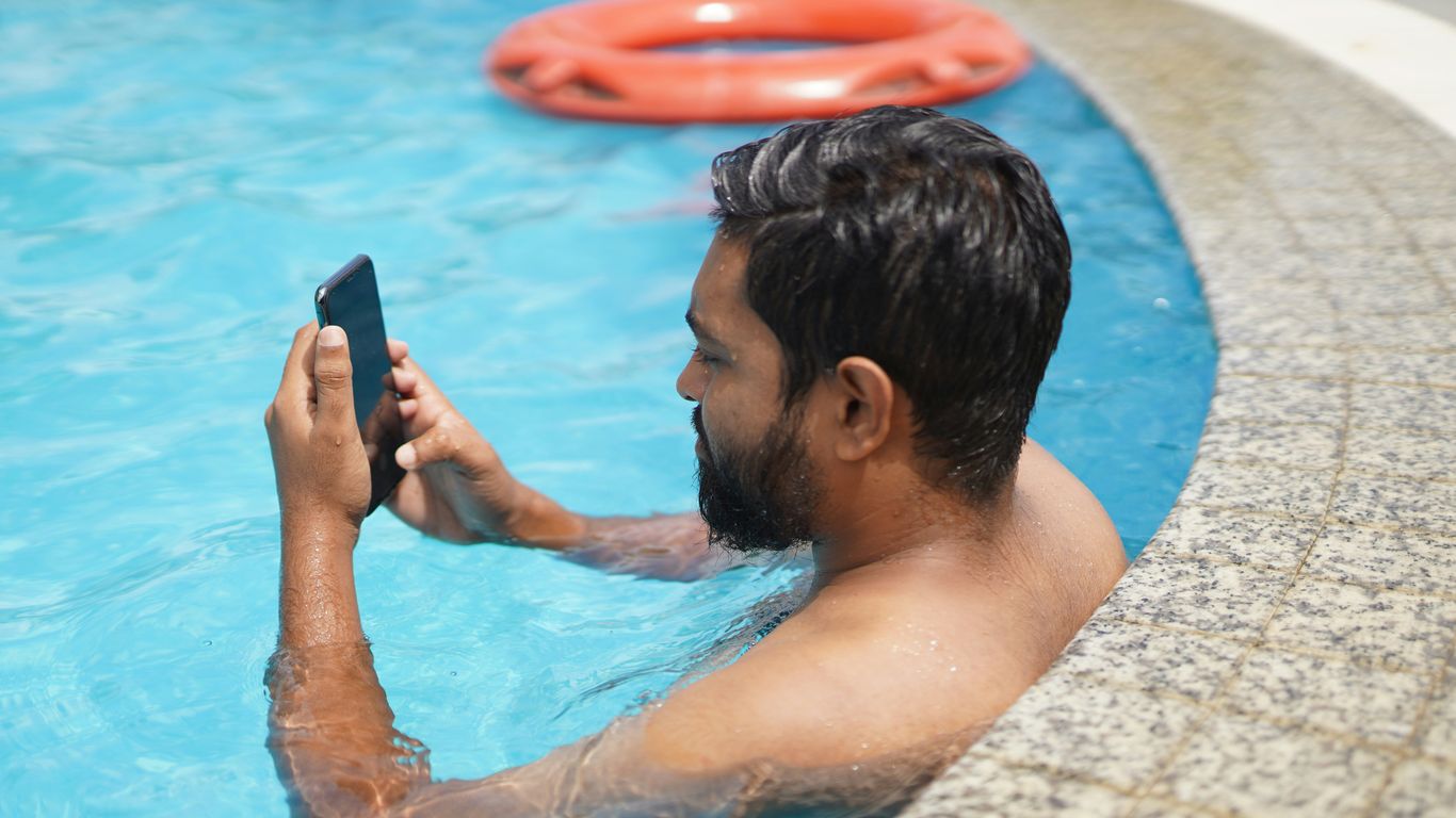 man in swimming pool holding smartphone