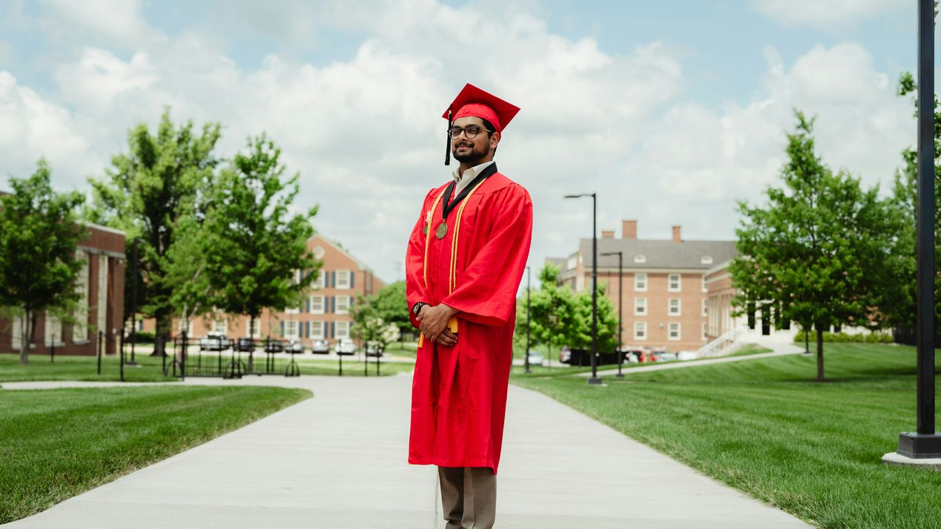 A man in a red graduation gown standing on a sidewalk