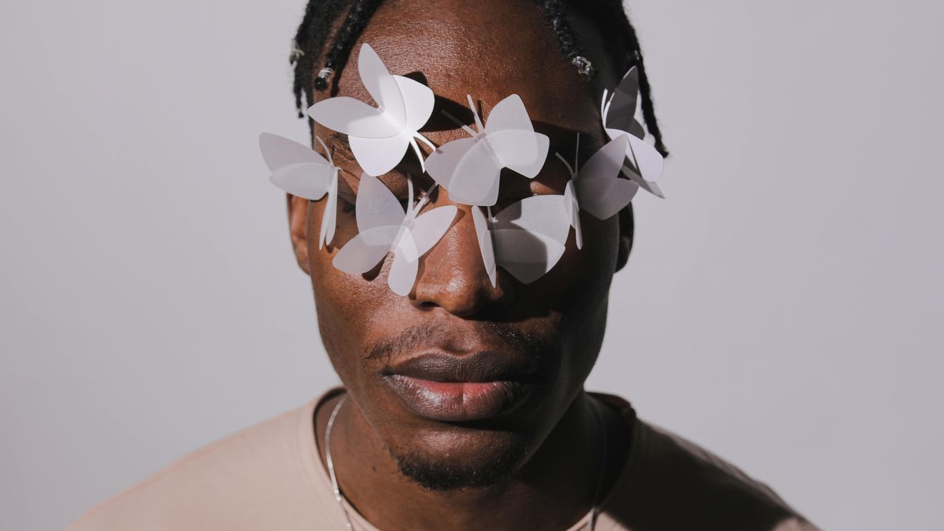Person with paper butterflies on face, neutral background, artistic style.