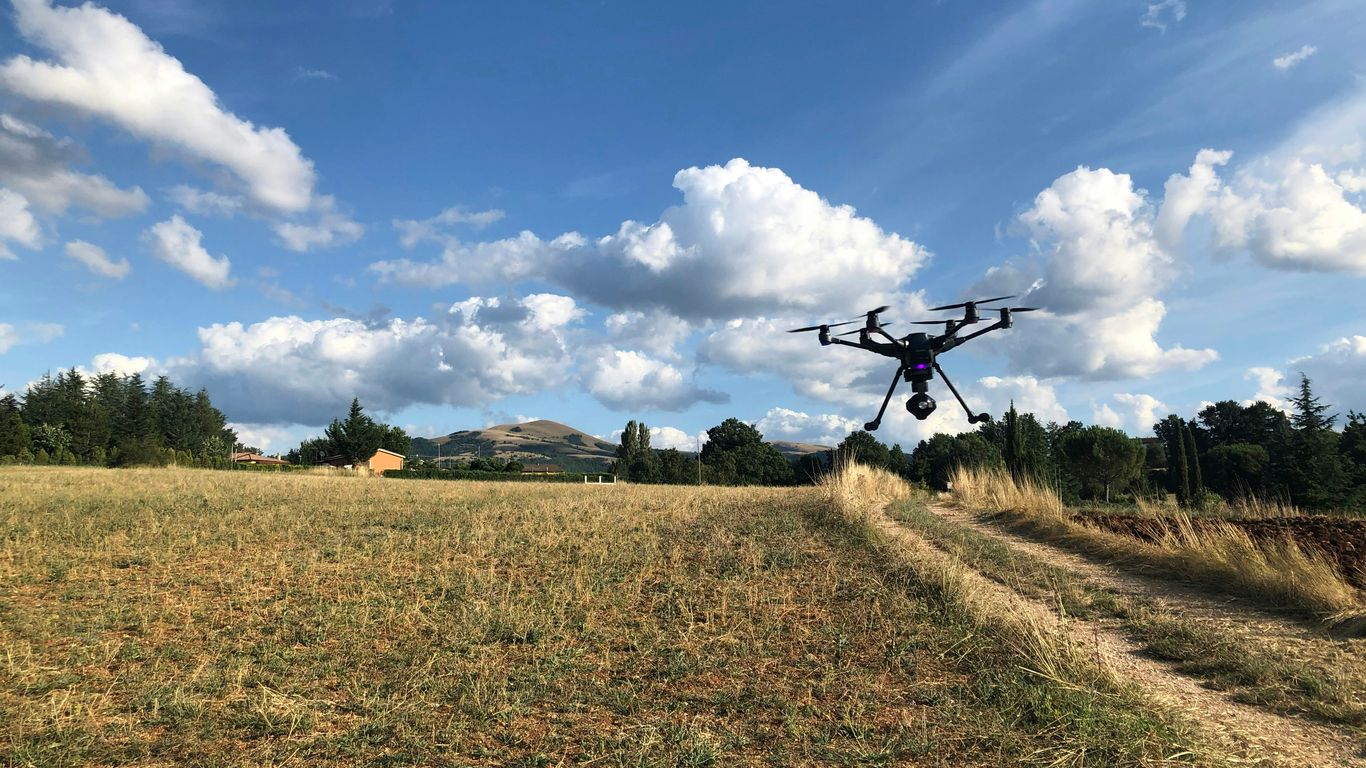 black drone near green field viewing mountain under blue and white skies during daytime