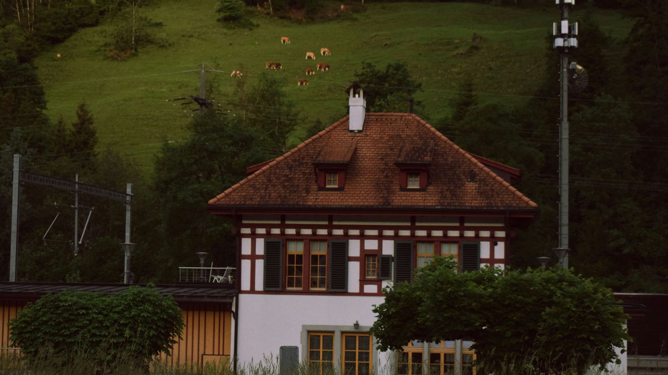 a white house with a brown roof in front of a lush green hillside