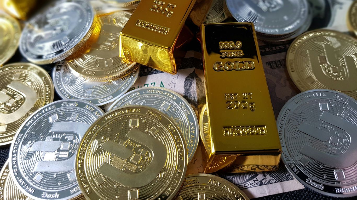 Gold bars and cryptocurrency coins atop currency notes.