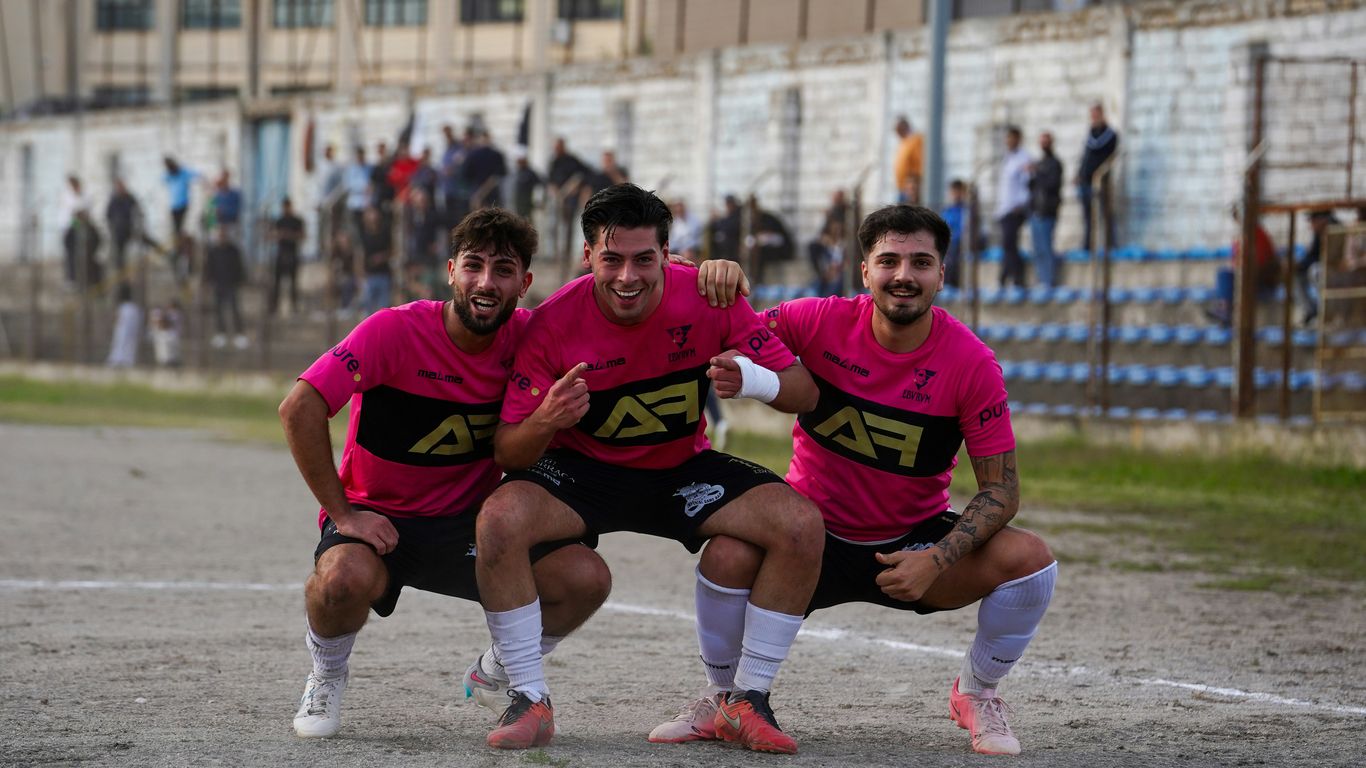 Three smiling soccer players in pink jerseys celebrating