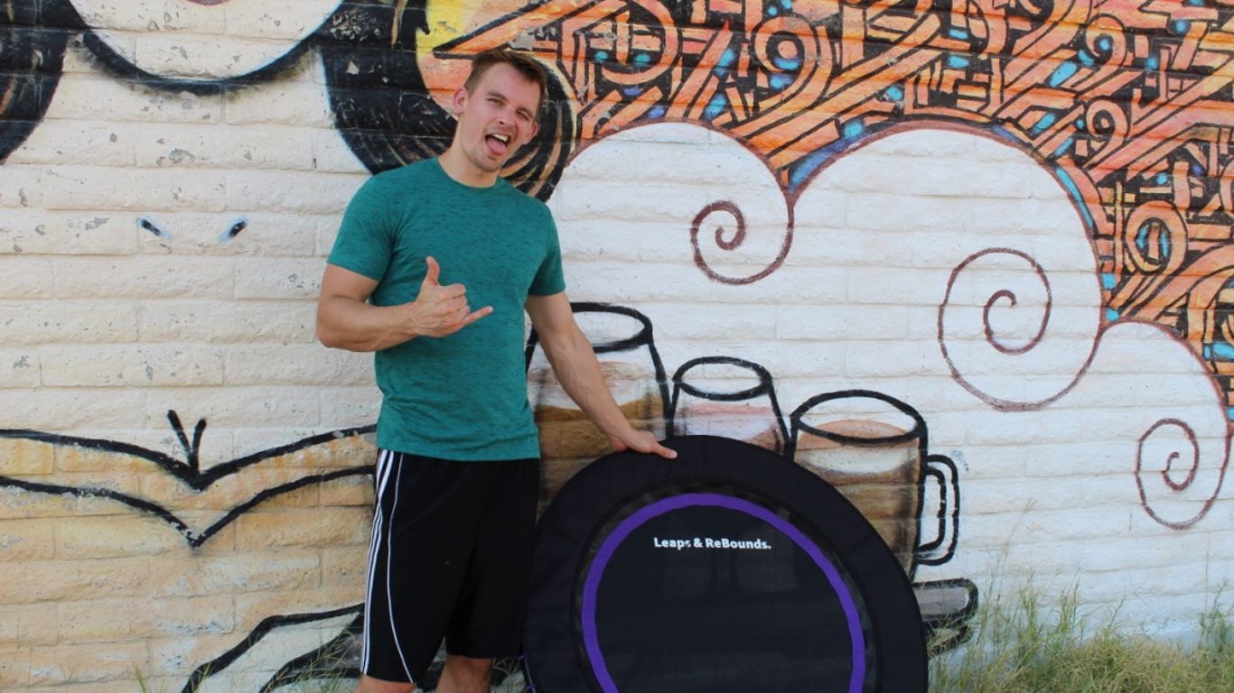 Person standing by a trampoline, colorful mural in background.