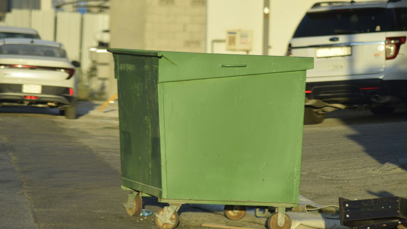 A large green dumpster on wheels in a street.