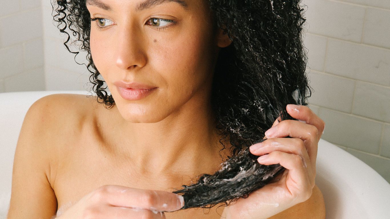 Person applying hair treatment while sitting in a bathtub.