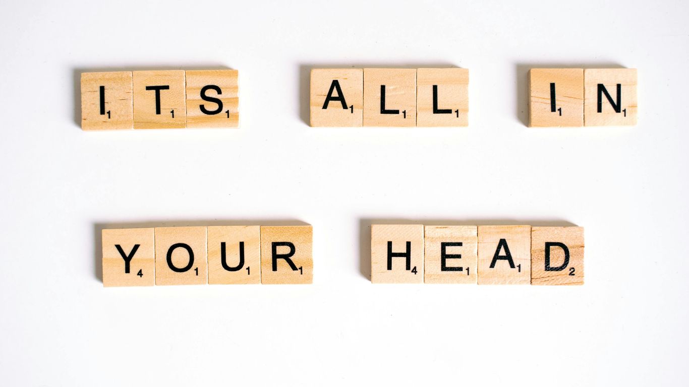 Wooden letter tiles spell 'ITS ALL IN YOUR HEAD' on white background.
