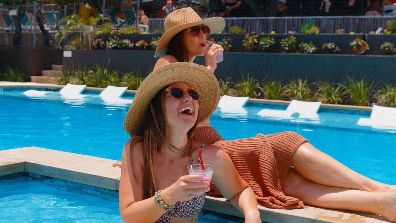 Two people enjoying drinks by a swimming pool on a sunny day.