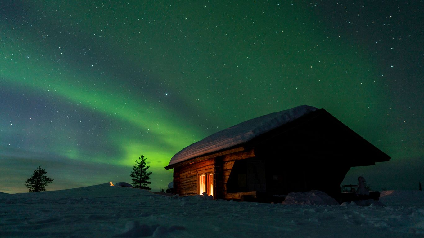 a cabin in the snow under a green aurora bore