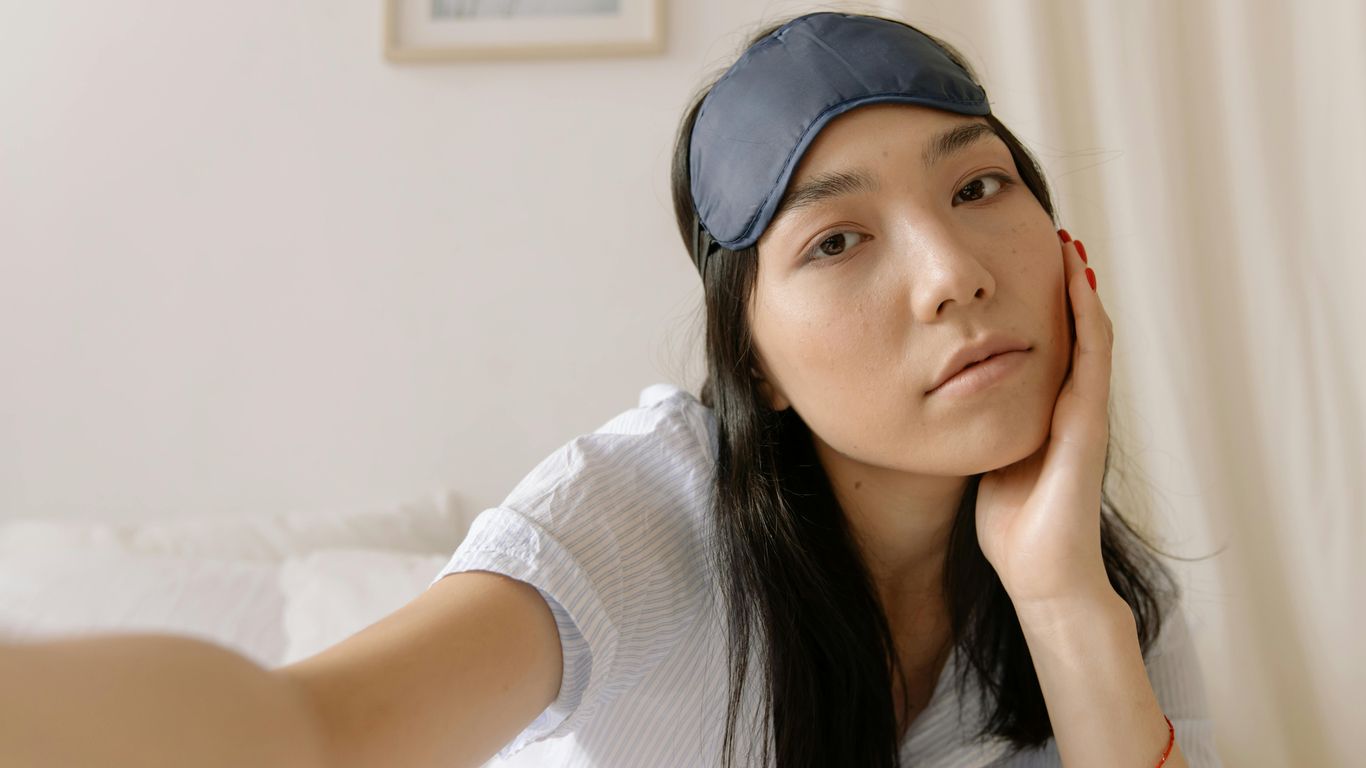 Person with sleep mask on head, sitting on bed, relaxed.