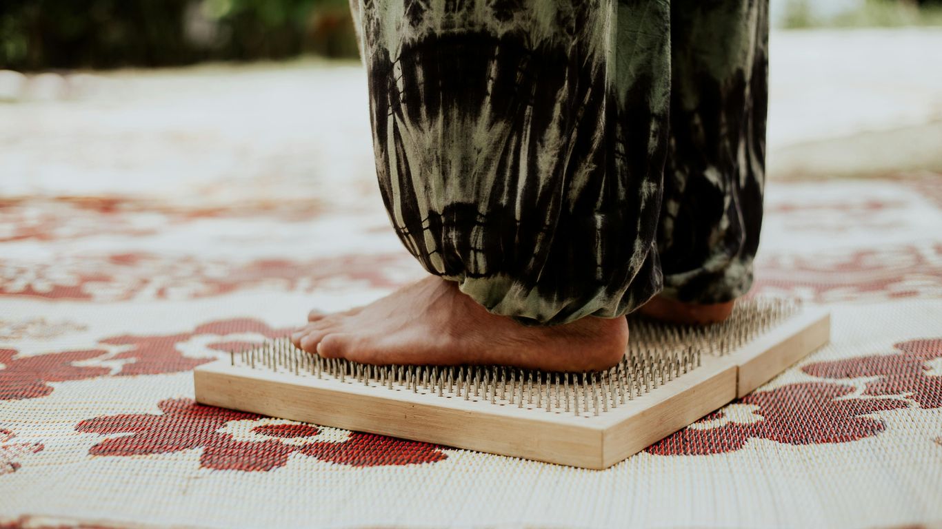 Person standing barefoot on a bed of nails, patterned mat underneath.