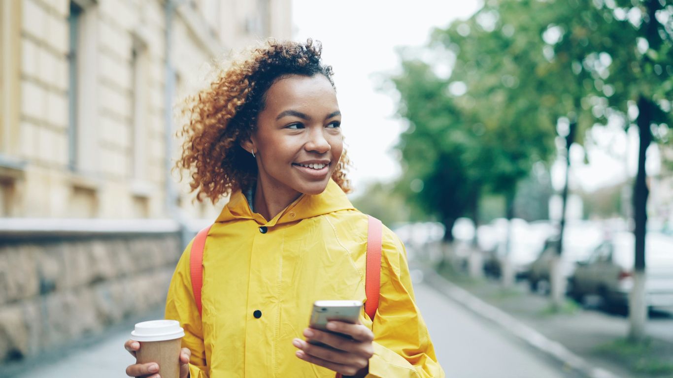 Woman in yellow raincoat holding coffee and phone