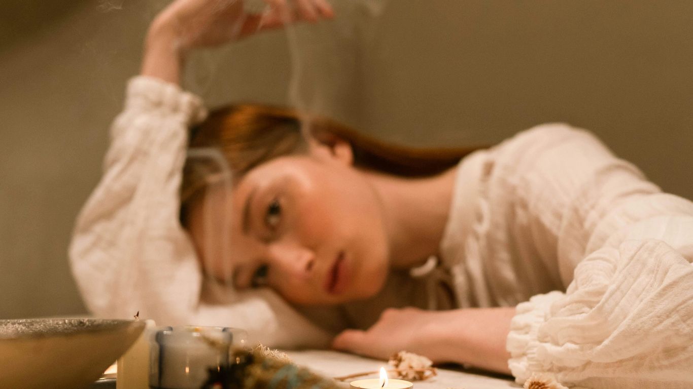Person resting head on table with candles and dried flowers.
